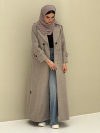 a woman wearing a beige Coat style abaya with lapel collar, Contrast black buttons, large patch pockets, cuff straps and matching sheila