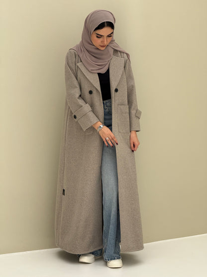 a woman wearing a beige Coat style abaya with lapel collar, Contrast black buttons, large patch pockets, cuff straps and matching sheila