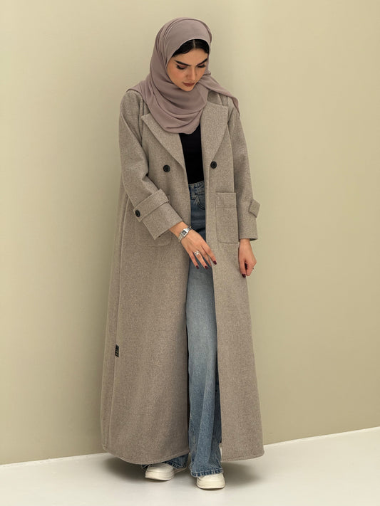 a woman wearing a beige Coat style abaya with lapel collar, Contrast black buttons, large patch pockets, cuff straps and matching sheila