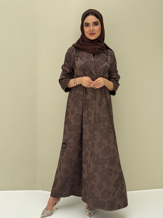 A woman wearing a chocolate brown abaya with a jacquard fabric, including a matching sheila headscarf, standing against a beige background.