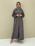 A woman wearing a steel grey abaya with a jacquard fabric, including a matching sheila headscarf, standing against a beige background.