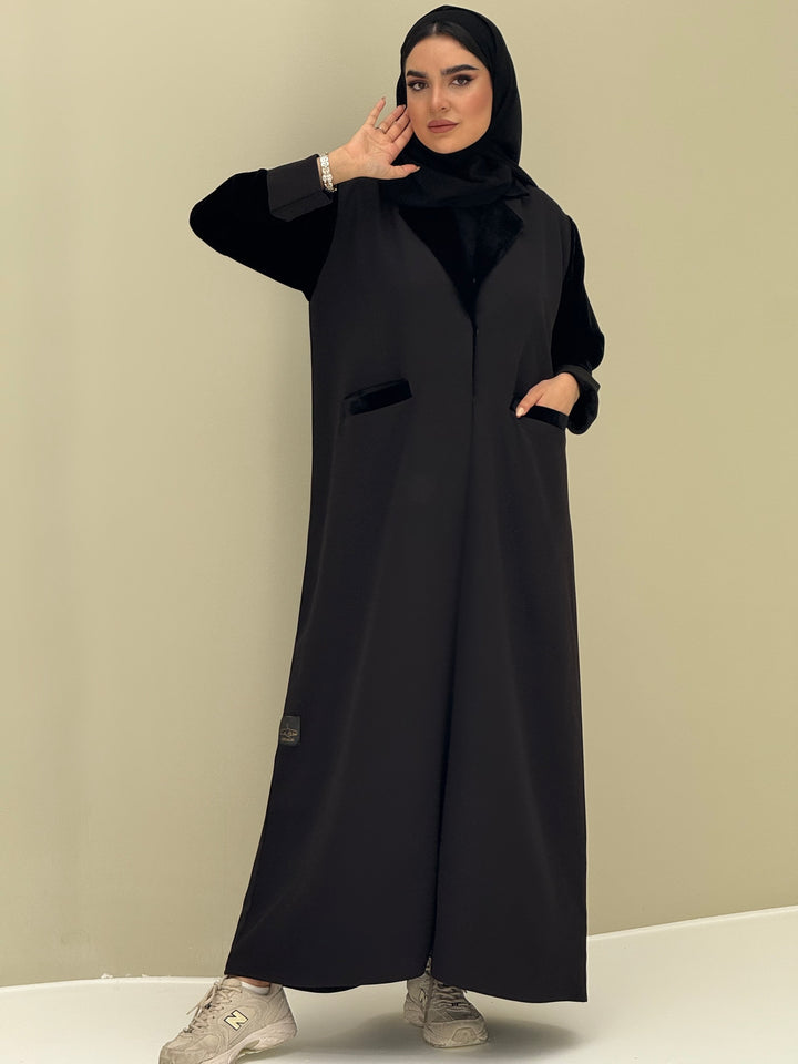 A woman wearing a black abaya with velvet and barbei fabric, posing against a neutral background.