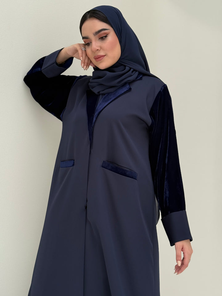 A woman wearing a navy blue abaya with velvet and barbei fabric, posing against a neutral background.
