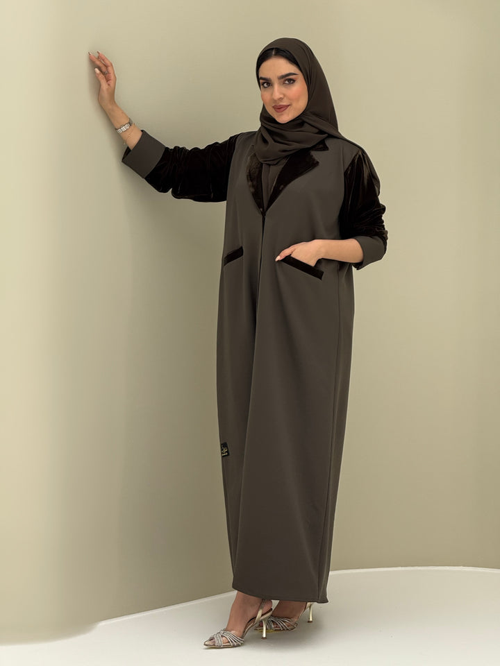A woman wearing a olive green abaya with velvet and barbei fabric, posing against a neutral background.