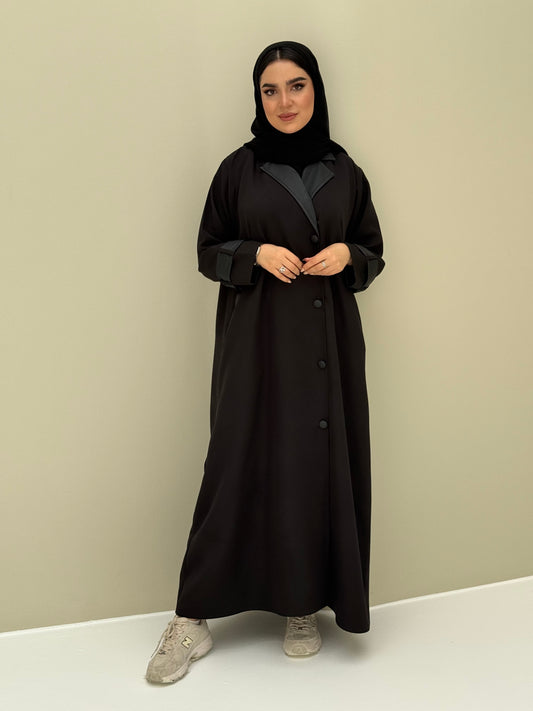 A woman wearing a black Coat style with lapel collar, with button details, and a matching sheila headscarf.