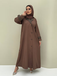 A woman wearing a brown Coat style with lapel collar, with button details, and a matching sheila headscarf.