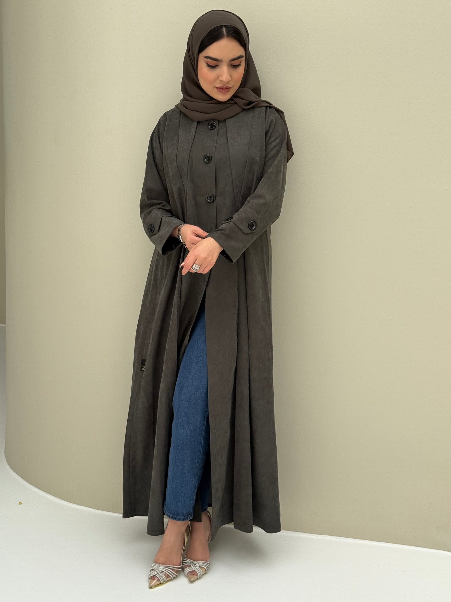 A woman wearing a dark olive Ice Cool Coat style with round neck and panel details Button-front, vertical bodice seams, buttoned cuff tabs
