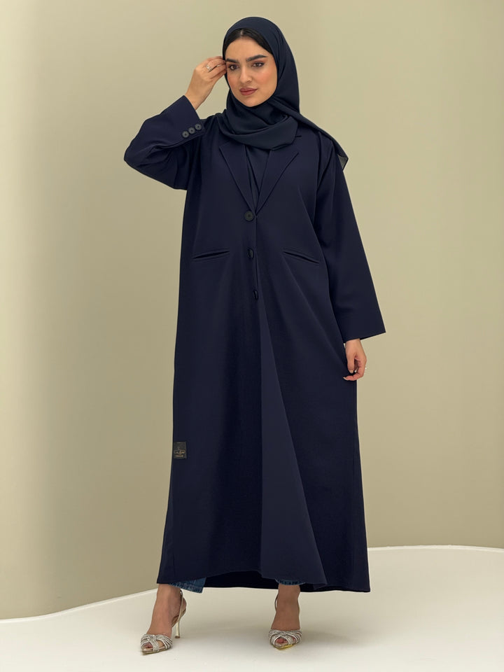 A woman wearing a navy blue Coat style with a lapel collar, Button-front, welt pockets, buttoned cuffs, and a matching sheila