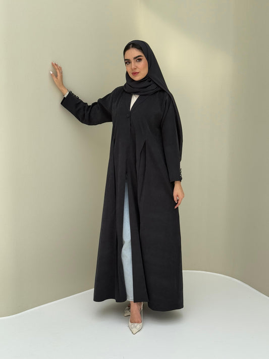 A woman standing in a neutral pose wearing a black Ice Cool Abaya flared coat style with lapel collar and a matching sheila, white shoes.