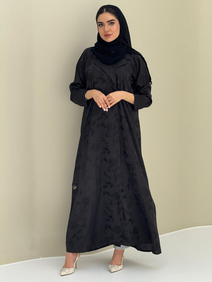 A woman wearing a black abaya with a tonal floral print pattern and a matching sheila headscarf.