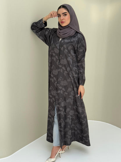 A woman wearing adaark grey abaya with a tonal floral print pattern and a matching sheila headscarf.