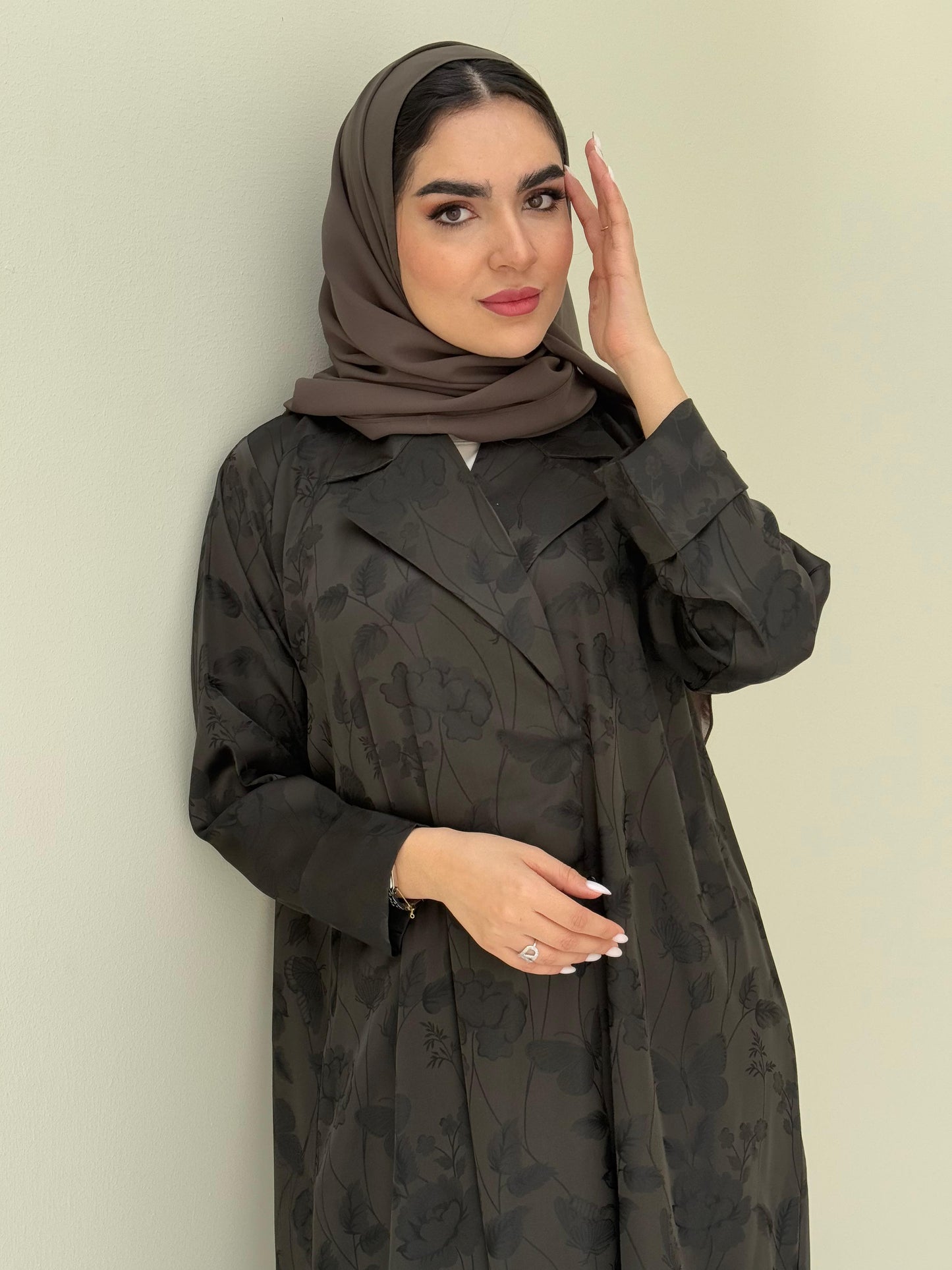 A woman wearing an olive green abaya with a tonal floral print pattern and a matching sheila headscarf.