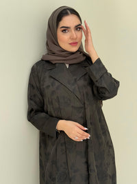 A woman wearing an olive green abaya with a tonal floral print pattern and a matching sheila headscarf.