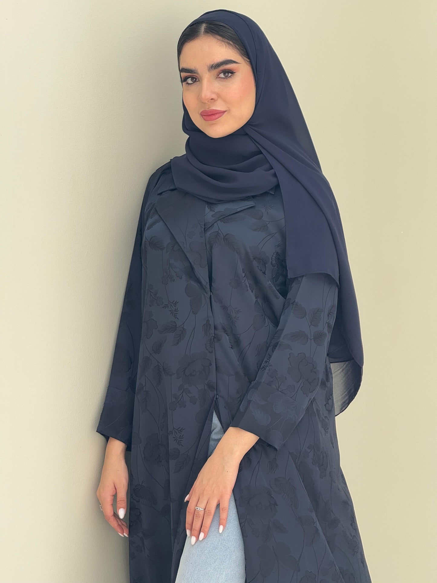 A woman wearing a navy blue abaya with a tonal floral print pattern and a matching sheila headscarf.