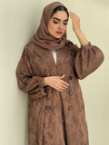 A woman standing in a room with cream background, wearing a bronze brown Abstract Satin abaya with Tonal brushstroke pattern, puffed cuffs, lapel collar, long sleeves and a matching Sheila headscarf