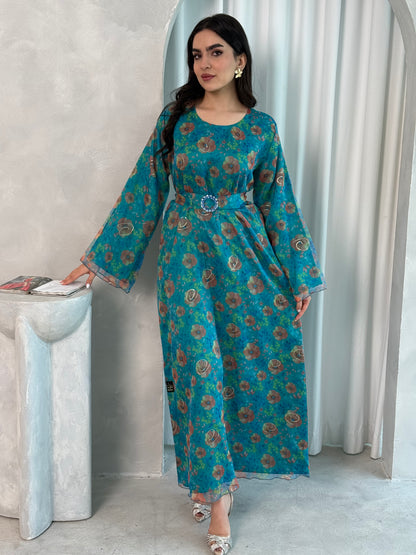 A woman wearing a Teal & Bronze printed organza (Lined) jalabiya dress with long sleeves and a belt, standing in front of a neutral backdrop.