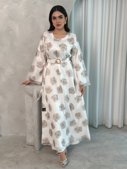 A woman wearing a White & Taupe printed organza (Lined) jalabiya dress with long sleeves and a belt, standing in front of a neutral backdrop.