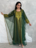 A person wearing a green and gold embroidered maxi dress with netting, posing indoors.