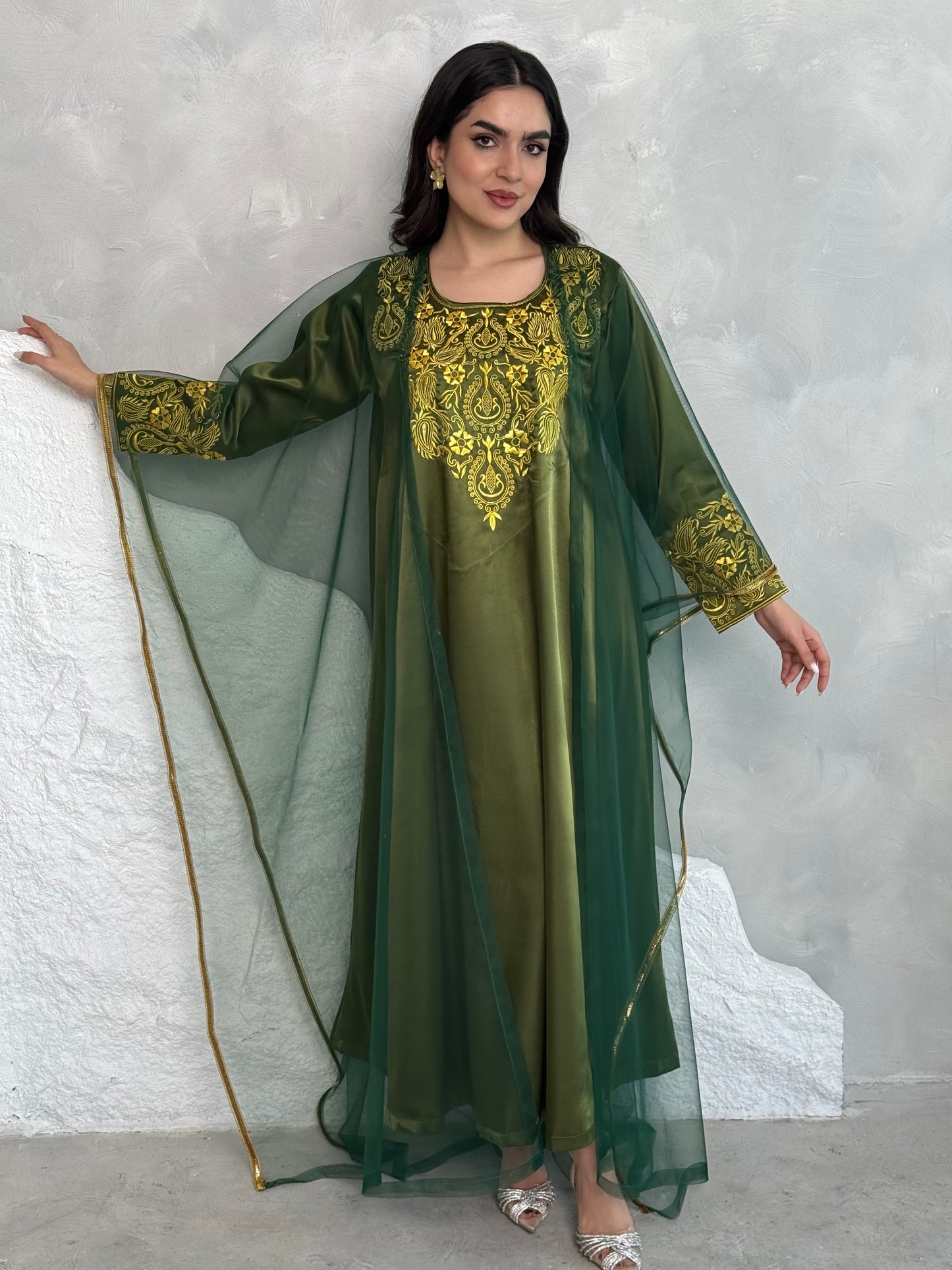A person wearing a green and gold embroidered maxi dress with netting, posing indoors.