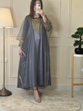 A person wearing a gray and gold embroidered maxi dress with netting, posing indoors.
