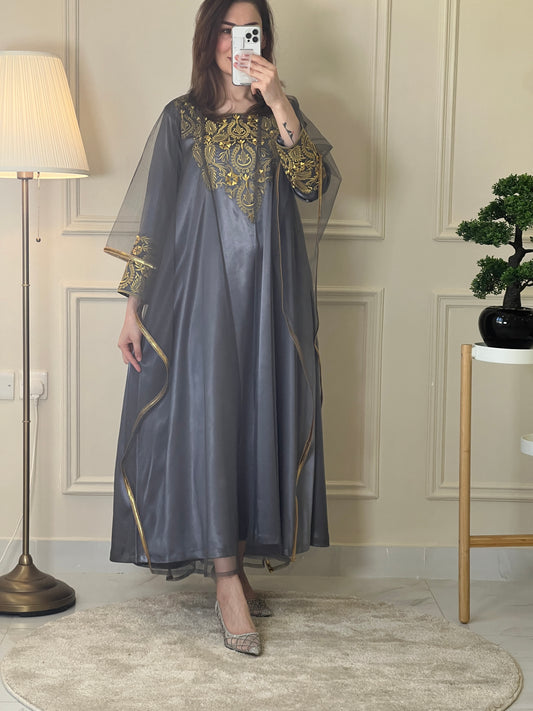 A person wearing a gray and gold embroidered maxi dress with netting, posing indoors.