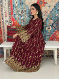 A woman seated on a bench against a colorful, patterned backdrop, wearing a maroon A-line Jalabiya with wide sleeves with gold embroidered details and long sleeves.