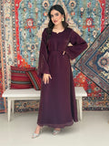 A woman standing in front of a decorative rug, wearing a purple Shimmer Organza dress with long sleeves and a belt, with her hair styled in an updo.