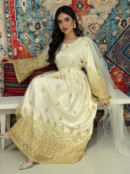 A woman sitting in front of a colorful backdrop wearing a cream and gold-colored Saree-Style Draped Jalabiya with net embroidery, featuring a belt.