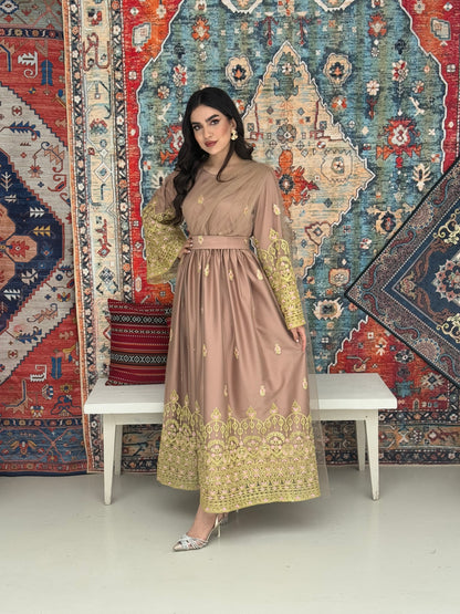 A woman standing in front of a colorful backdrop wearing a dusty rose and gold-colored Saree-Style Draped Jalabiya with net embroidery, featuring a belt.