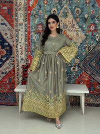 A woman standing in front of a colorful backdrop wearing a sage green and gold-colored Saree-Style Draped Jalabiya with net embroidery, featuring a belt.