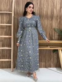 A woman sitting in a tropical setting wearing a grey Sheer Net Overlay with gold Floral Embroidery dress and a belt.