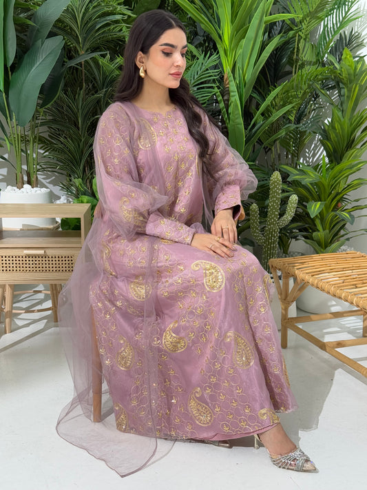 A woman seated in a garden setting, wearing an A-line dusty pink Paisley Dress with Bishop Sleeves with gold embroidery and a netted veil.