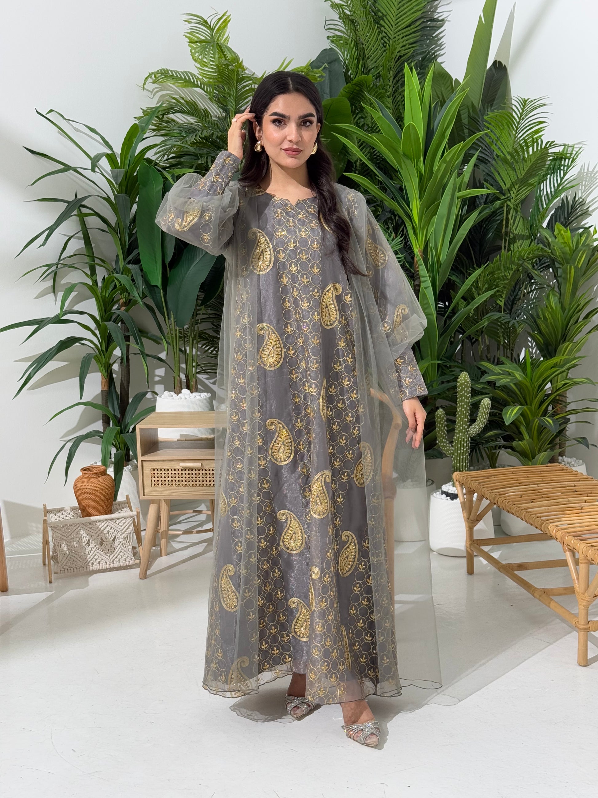 A woman seated in a garden setting, wearing an A-line grey Paisley Dress with Bishop Sleeves with gold embroidery and a netted veil.