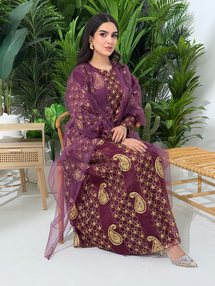 A woman seated in a garden setting, wearing an A-line Maroon Paisley Dress with Bishop Sleeves with gold embroidery and a netted veil.