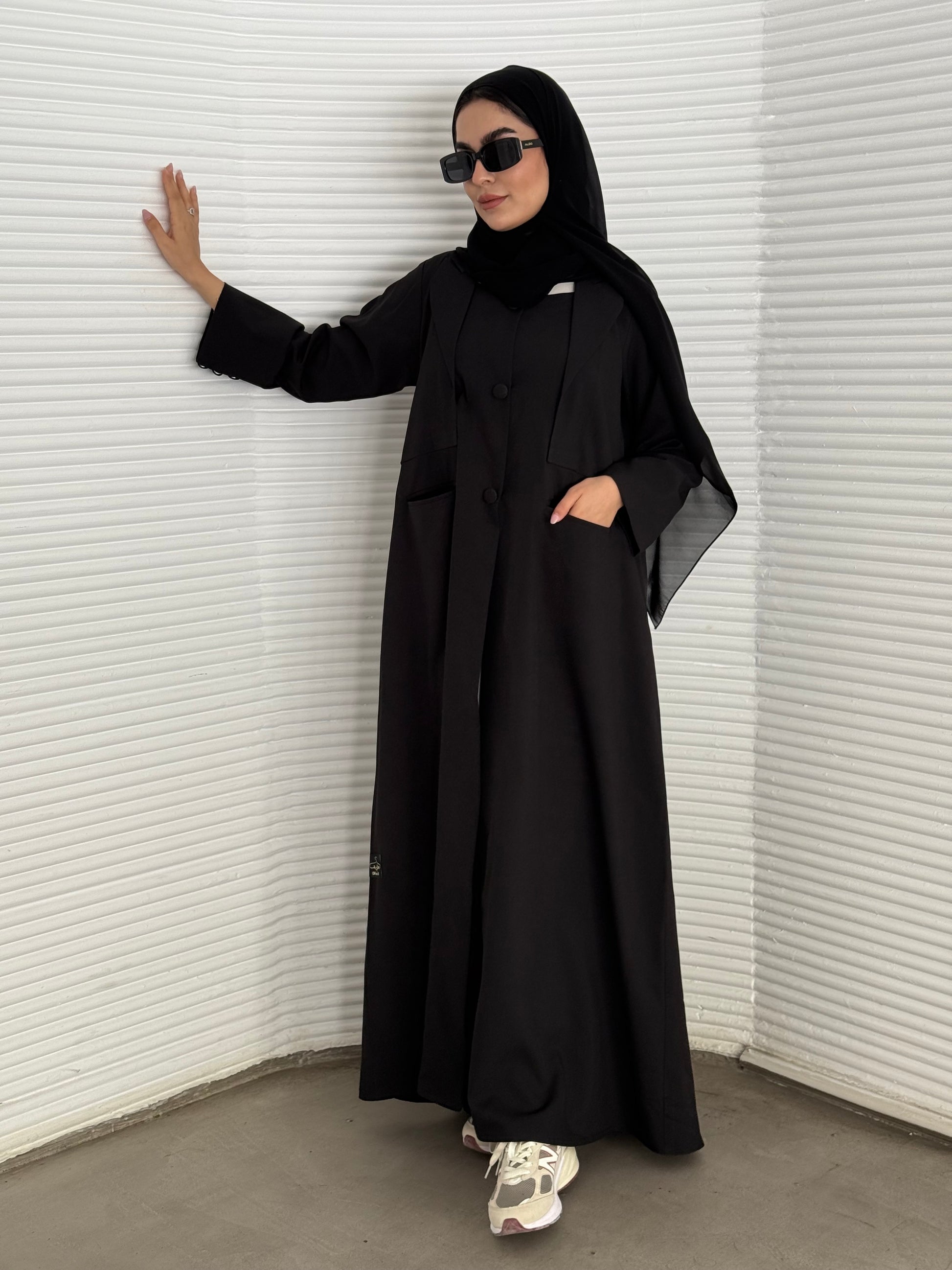 A black abaya, tailored from Linen, it features a coat-style collar and pockets for a structured fit.