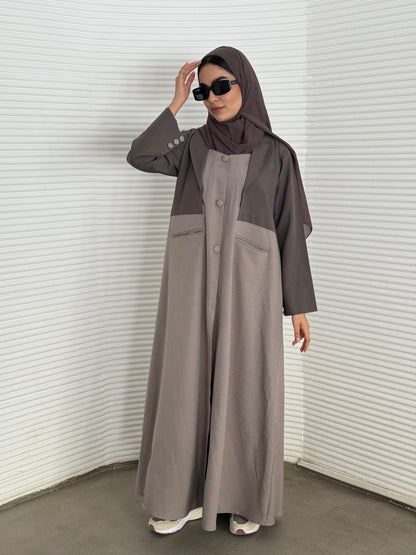 A taupe and beige abaya, tailored from Linen, it features a coat-style collar and pockets for a structured fit.