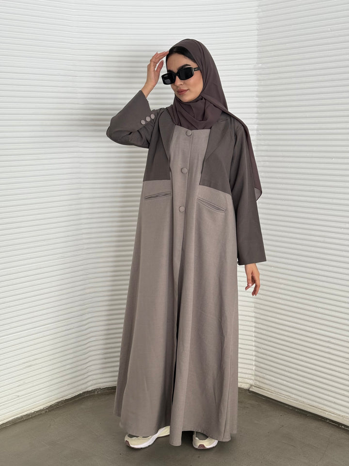 A taupe and beige abaya, tailored from Linen, it features a coat-style collar and pockets for a structured fit.