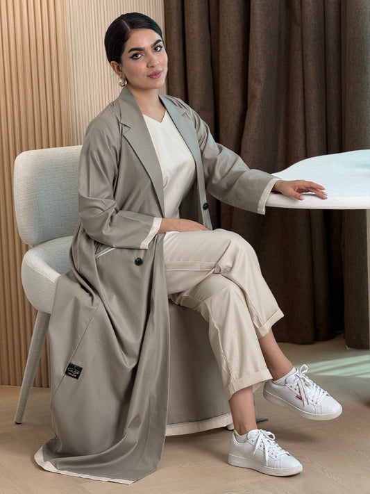 Woman sitting on a chair wearing a long Light Grey Linen Abaya Set, white sneakers, and beige pants.