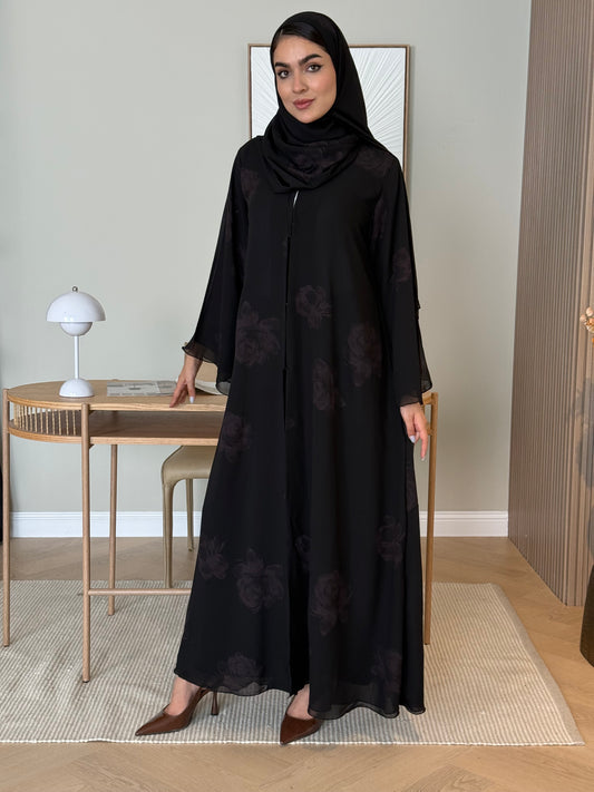 Woman wearing a Black & dark maroon abaya with floral patterns and a matching sheila in a minimalistic setting.