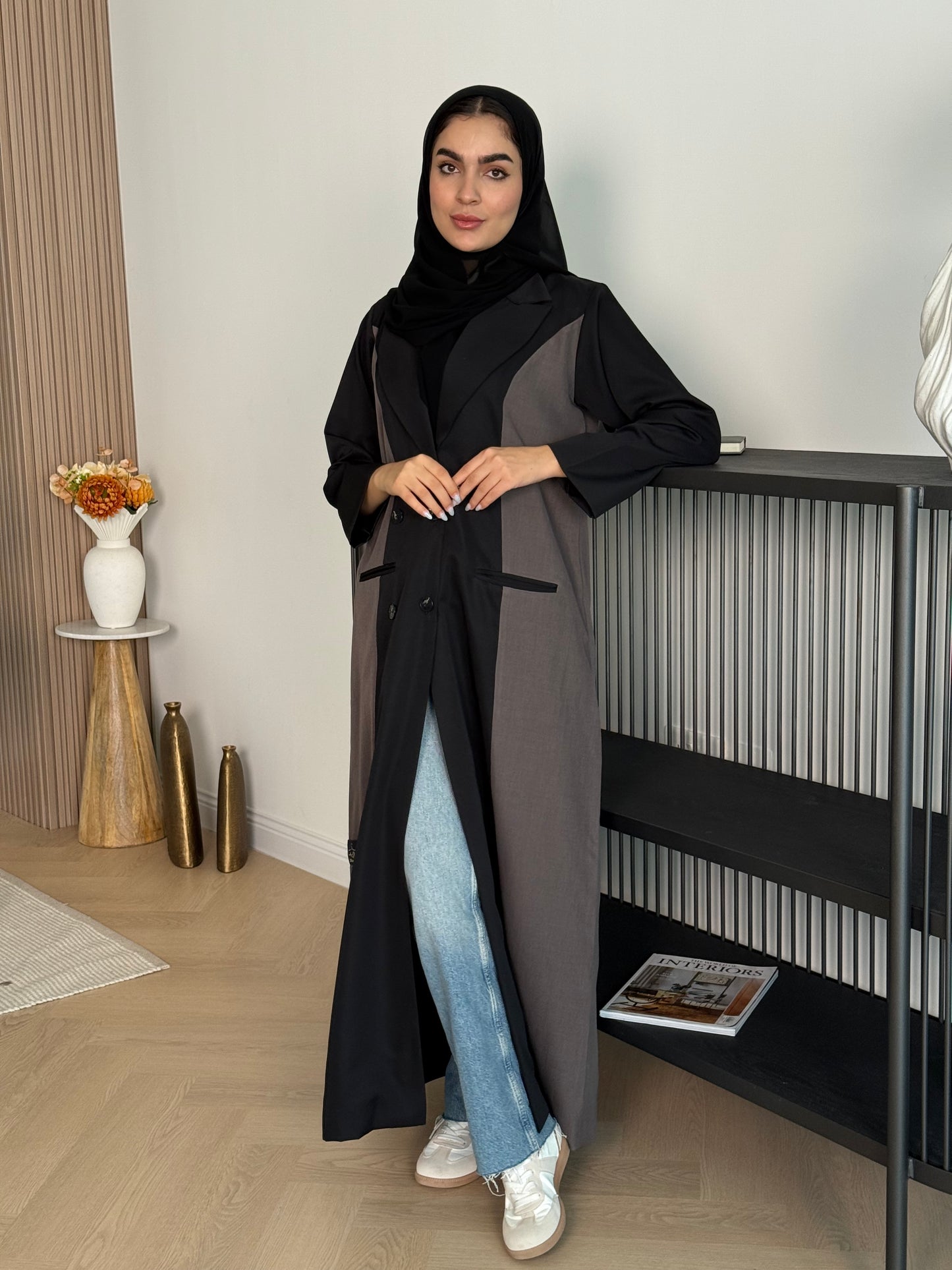 Woman in a long Black & Taupe Linen Coat Abaya with a matching sheila standing in a room with a desk and chair.