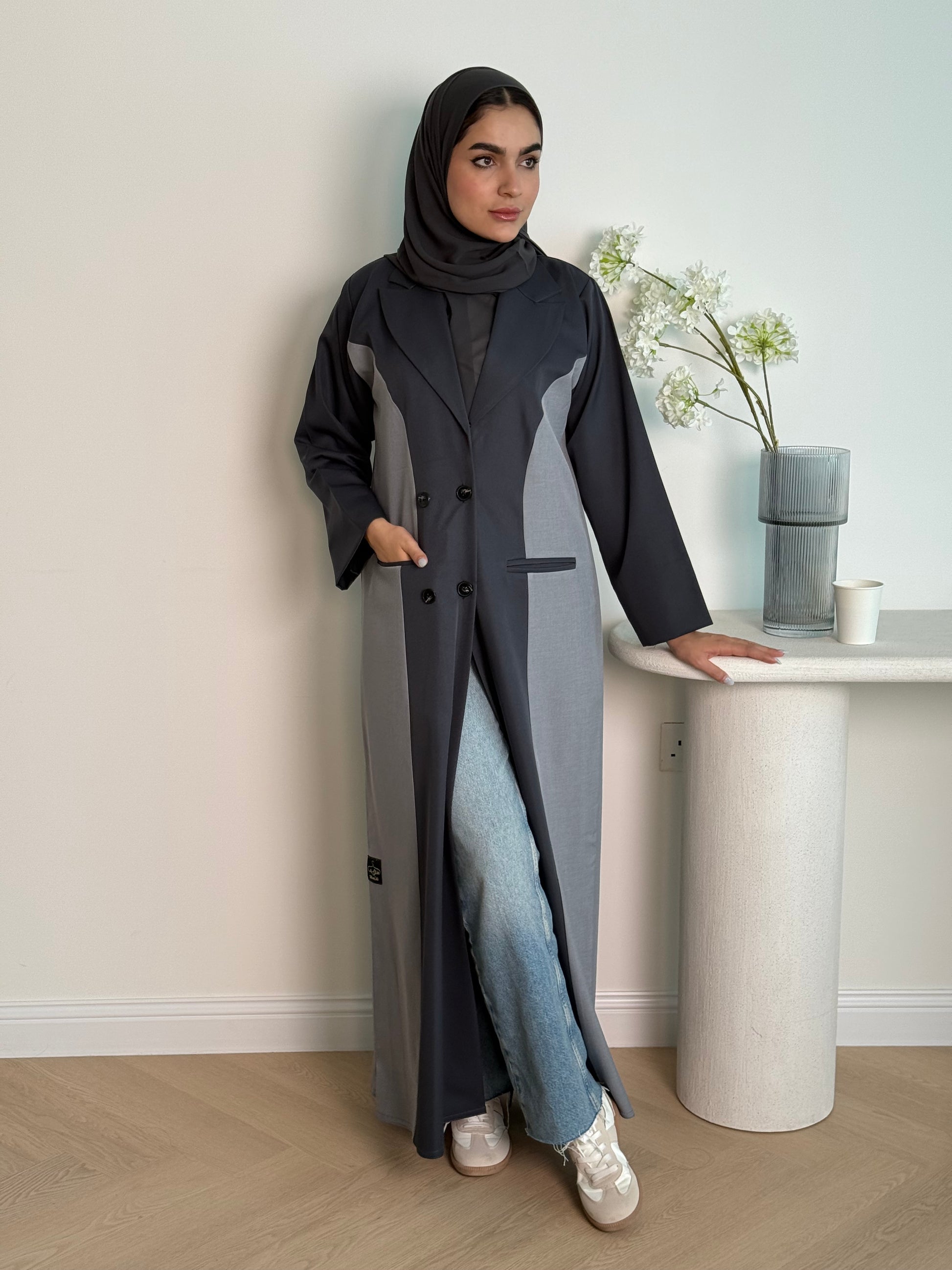 Woman in a long dark grey Linen Coat Abaya with a matching sheila standing in a room with a desk and chair.