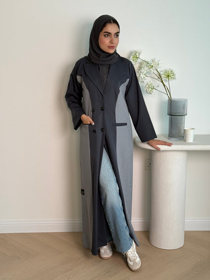 Woman in a long dark grey Linen Coat Abaya with a matching sheila standing in a room with a desk and chair.