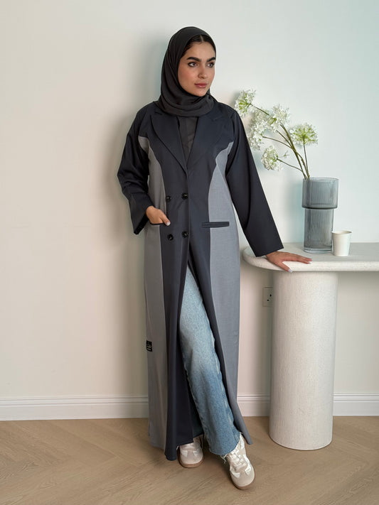 Woman in a long dark grey Linen Coat Abaya with a matching sheila standing in a room with a desk and chair.