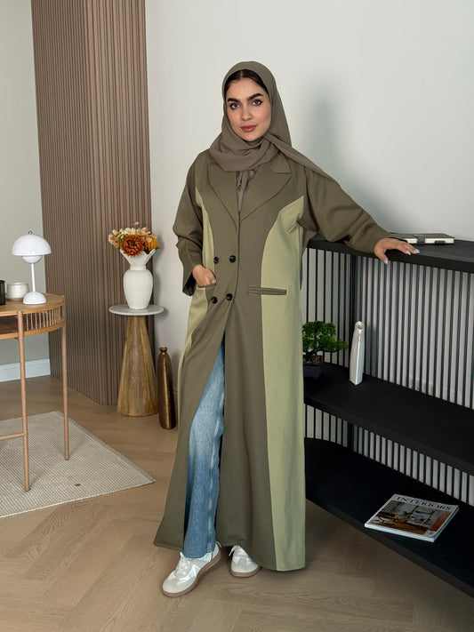 Woman in a long Olive Green Linen Coat Abaya with a matching sheila standing in a room with a desk and chair.
