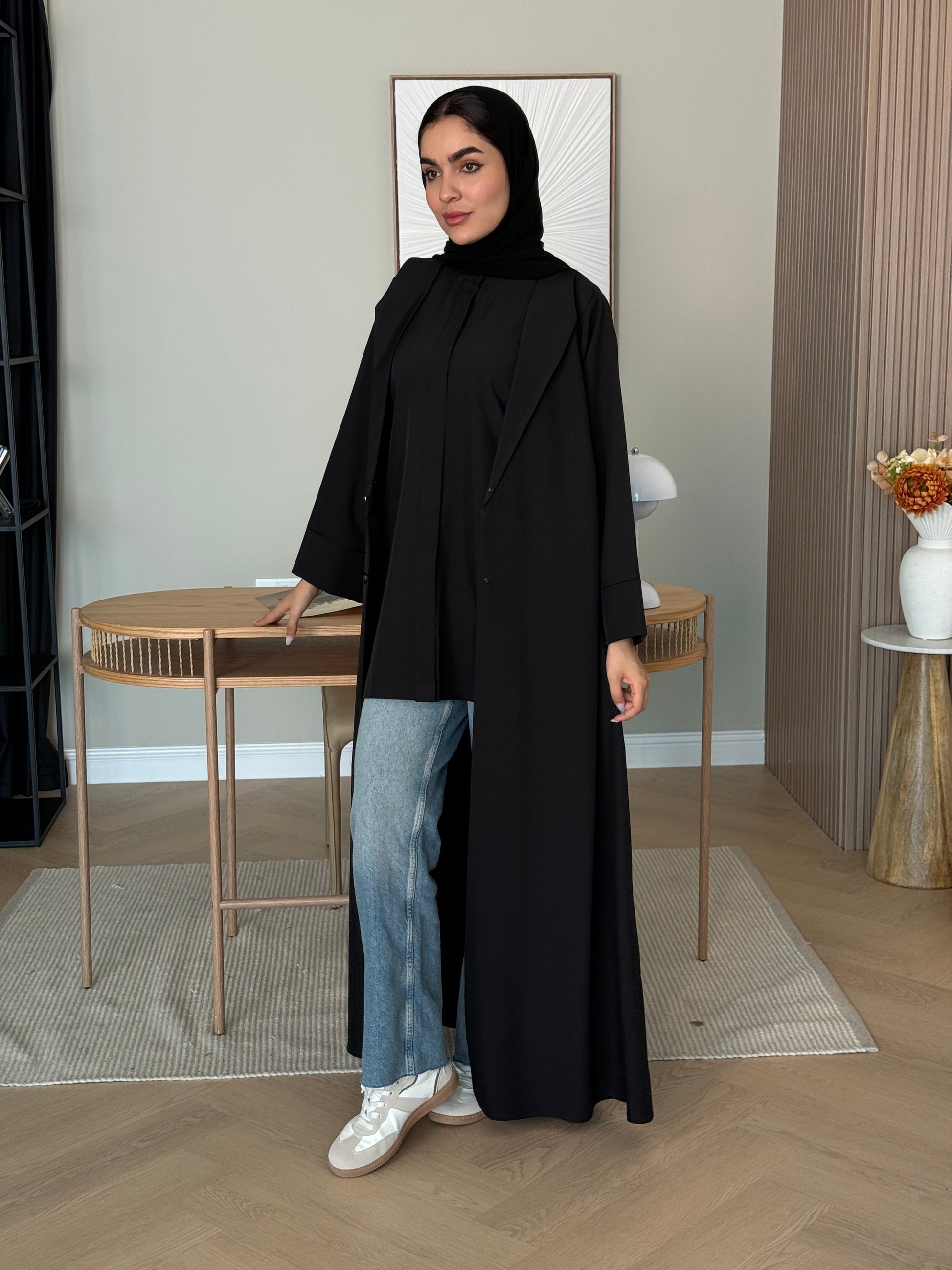 Woman wearing a long Black Linen Coat Abaya with matching Sheila standing indoors.