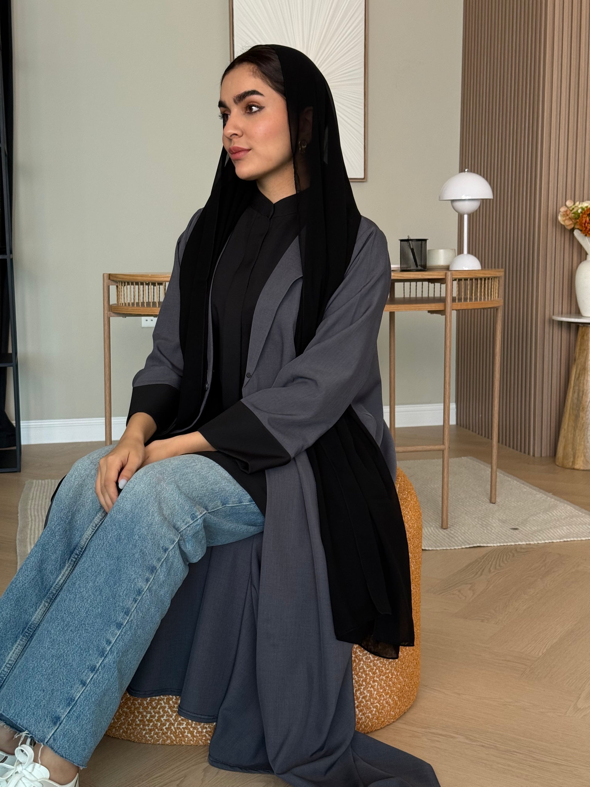Woman sitting on a chair wearing a Dark Grey Linen Coat Abaya in an indoor setting with a black sheila 