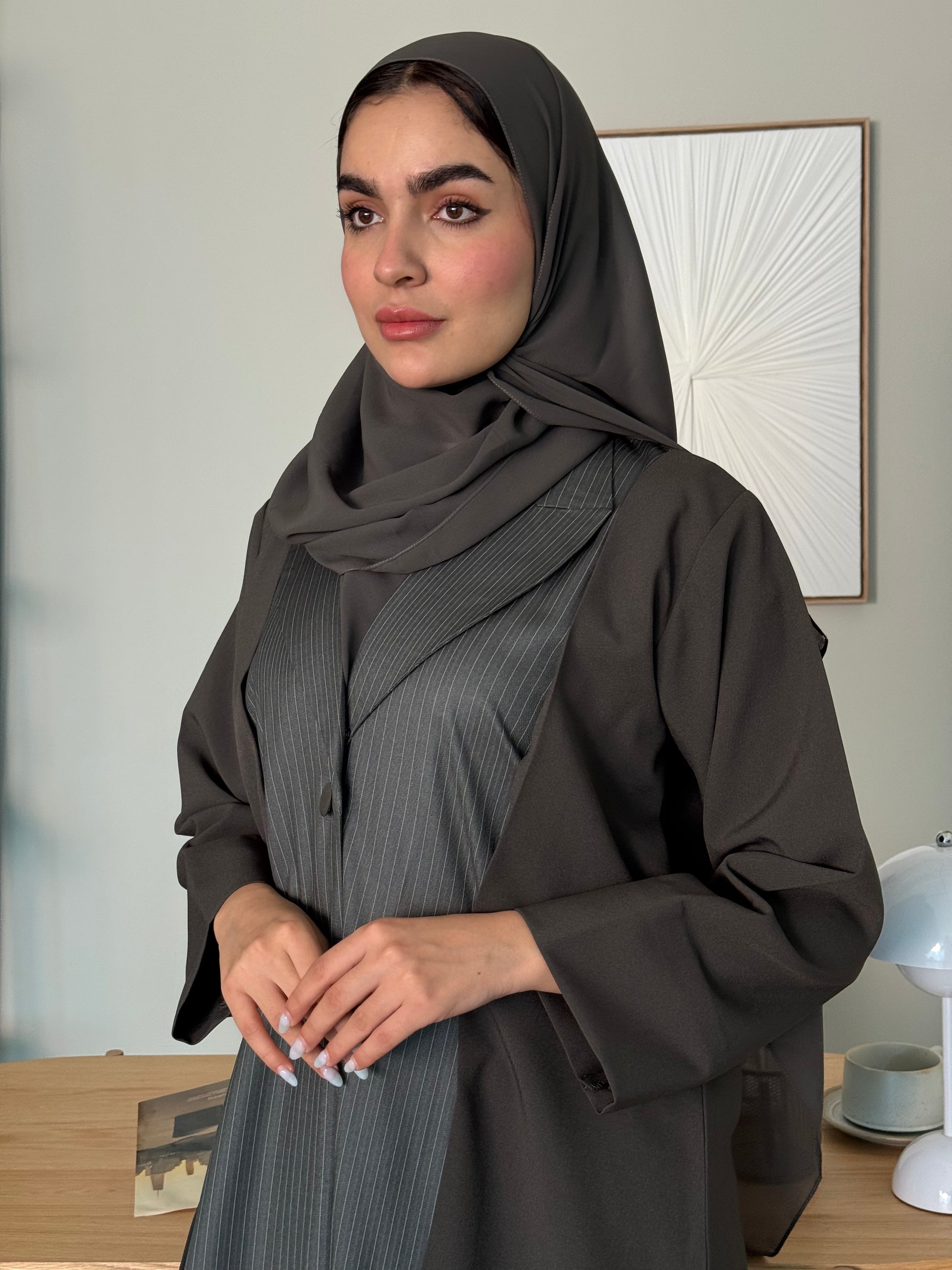 Person wearing a long  Dark olive green Pinstripe Linen Abaya with a matching sheila standing in a room with a mirror.