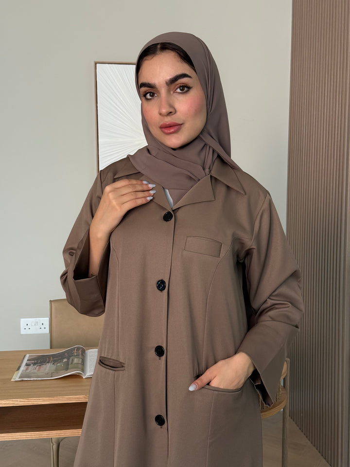 Woman wearing a brown Linen Pocket Abaya coat  with a matching sheila in an indoor setting