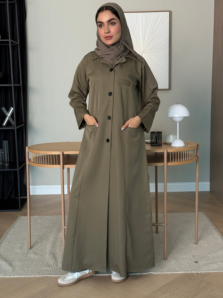 Woman wearing an olive green Linen Pocket Abaya coat  with a matching sheila in an indoor setting