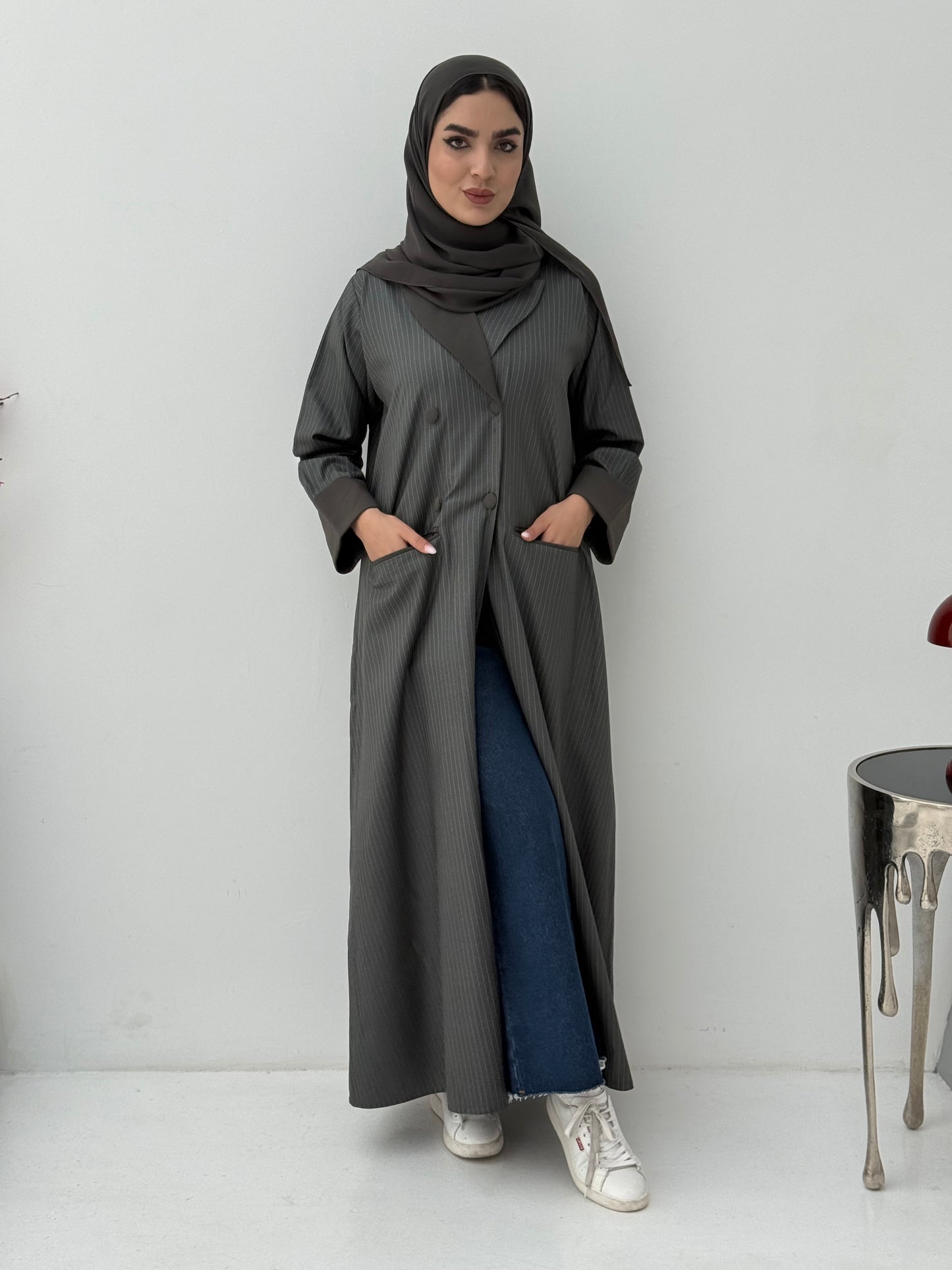 Woman wearing a long Dark Olive Pinstripe Linen Coat Abaya with a hood against a white background